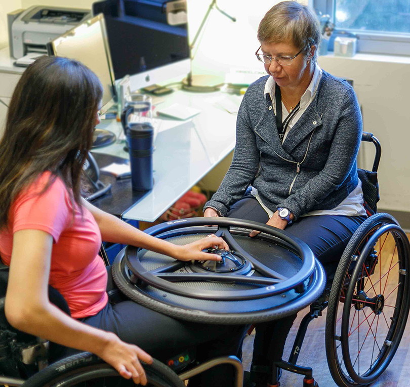 Two researchers examining a wheel innovation for a wheelchair