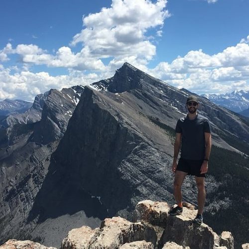 man standing on mounain peak with mountain range in background