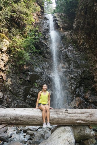 woman sitting on log in front of waterfall